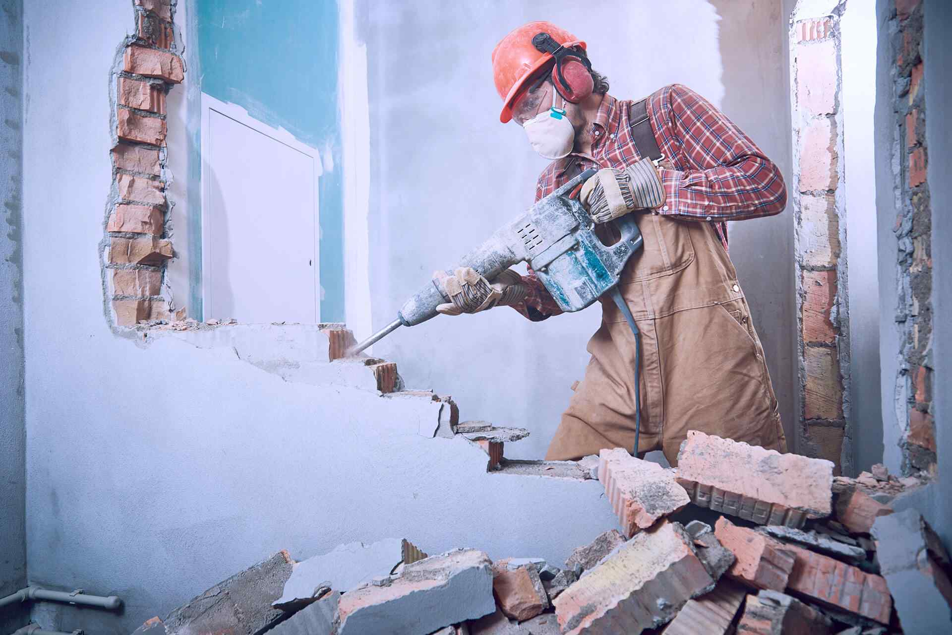 Worker using equipment to demolish a brick interior wall.