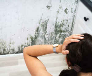 Woman holding her head while looking at a mold in a wall