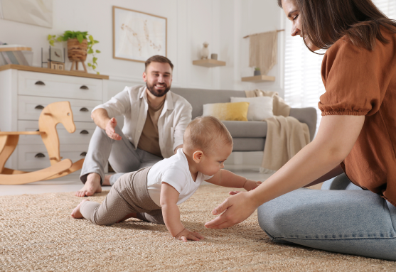 Parent and their crawling baby on a carpeted floor.